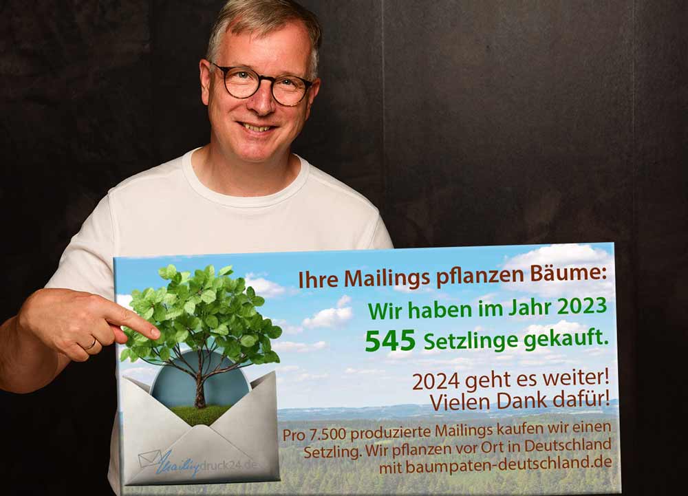 Uwe Fenner vom Mailingservice mailingdruck24 hält ein Schild mit der Aufschrift - Ihre Mailings pflanzen Bäume  